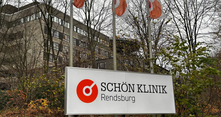 Foto der Schön Klinik in Rendsburg im Winter. Im Vordergrund ist das Klinik-Logo auf einem Schild zu sehen.